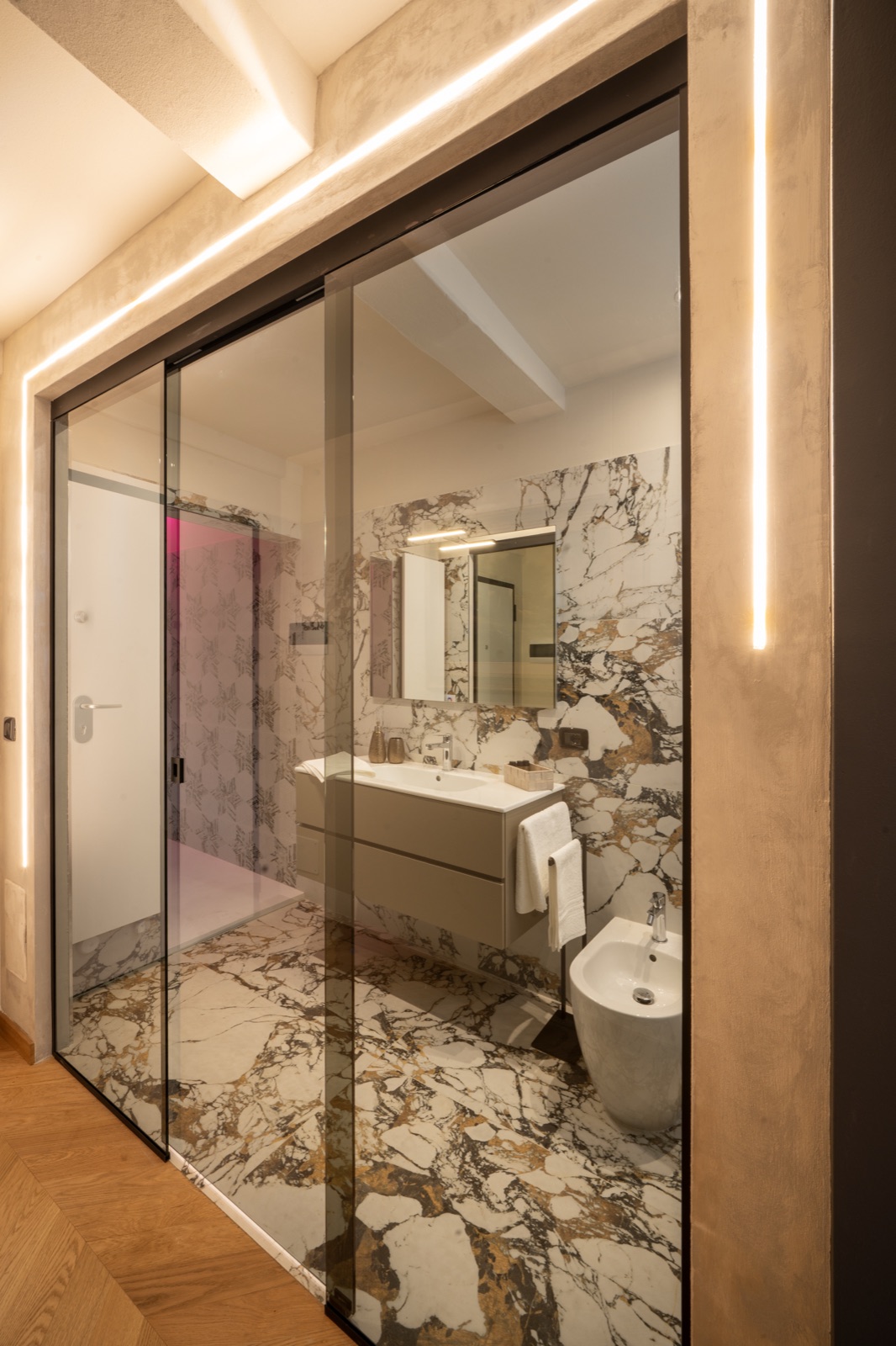 La porta scorrevole in vetro del bagno in marmo, con il lavabo e lo specchio