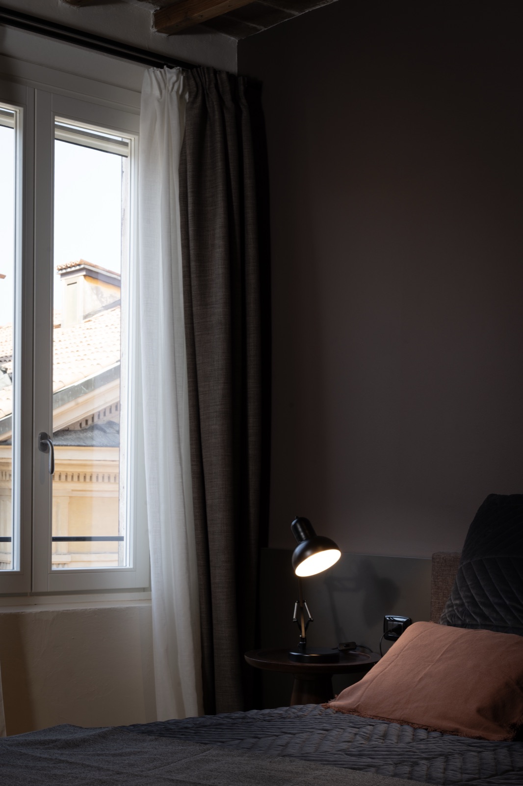 Il letto e la lampada da lettura accanto alla finestra, in penombra
