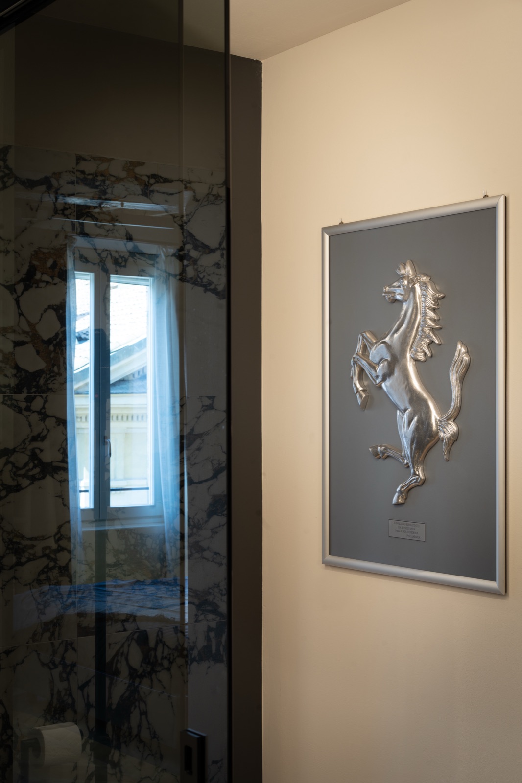 Il quadro del cavallino rampante accanto alla doccia in vetro e marmo
