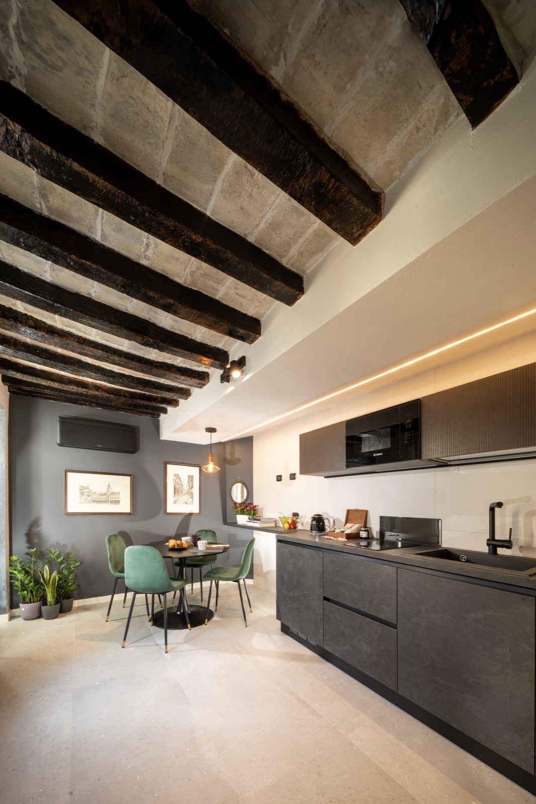 The kitchen beneath the dark beams, with the table and green chairs
